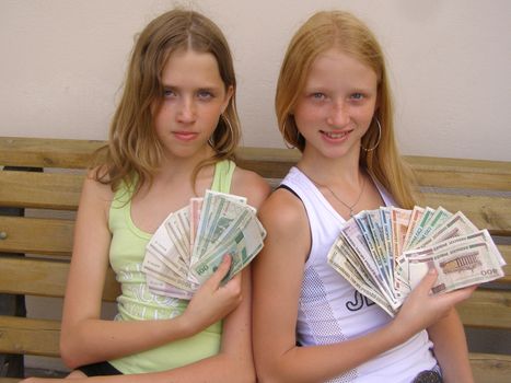 two girls sit on bench and hold in the hands Byelorussian rubles. 
