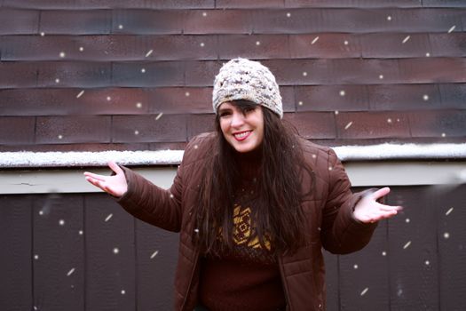 Attractive woman playing outside in the snow. Woman wearing winter clothing outside standing next to a wooden cabin.