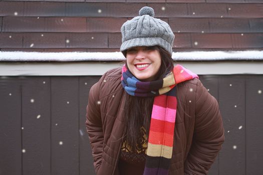 Attractive woman playing outside in the snow. Woman wearing winter clothing outside standing next to a wooden cabin.