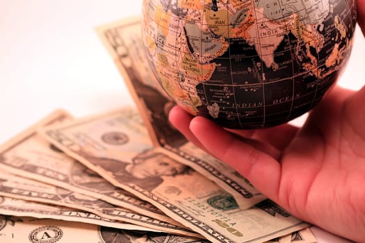 World globe and US money against white background. Hand holding the globe over the money. Business, trade, commerce, economy and finance for the world.
