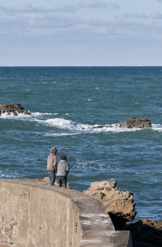 Two fishermen on a concrete jetty with sea and sky in the background