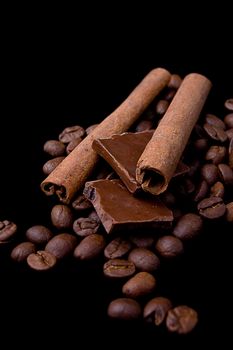 Cinnamon sticks over coffee beans and chocolate on black