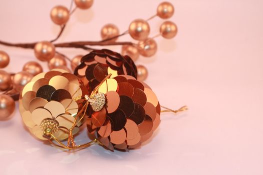 Metallic bronze and gold Christmas ornaments and berries against soft pink background. Holiday decorations for the season.