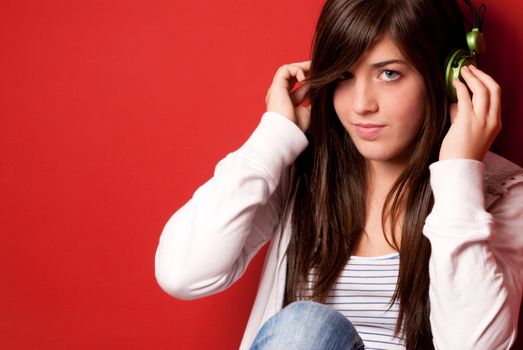 Young girl listening music with headphones on a red wall