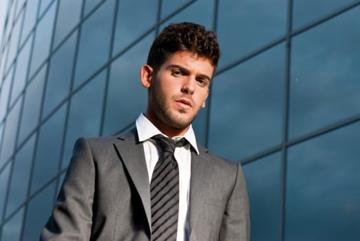 Young businessman looking to camera on modern building background