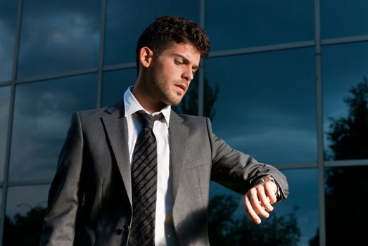 Young businessman looking clock at night on modern building background