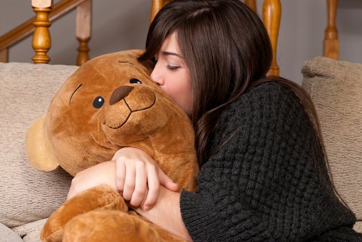 Young woman embracing and kissing teddy bear sitting on sofa close-up