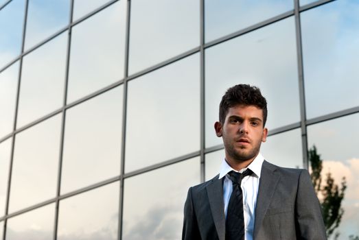 Young businessman looking to camera on modern building background