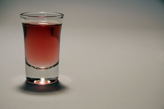 small glass of red alcohol, grey background