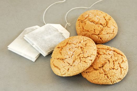 three fresh appetizing oatmeal cookies with tee bags over gray background