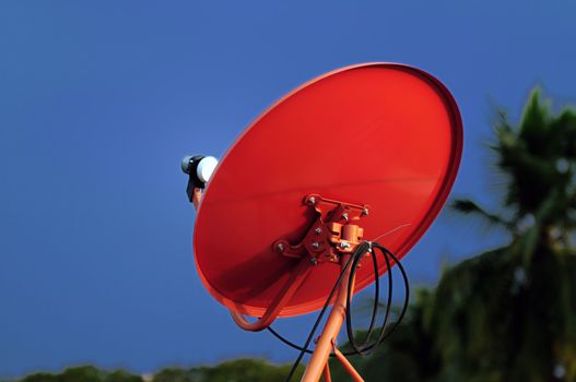 A red satellite dish against the blue sky background