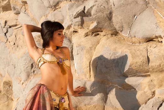 Sexy belly dancer posing against sunlit rocks