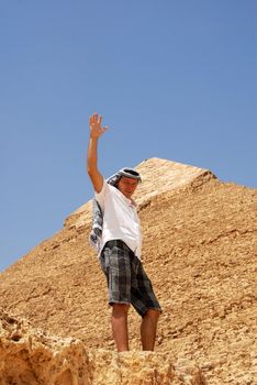 caucasian man tourist in arabic kerchief standing by pyramids on Giza in Egypt, waving