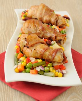 roast chicken leg wrapped in bacon with vegetables