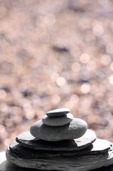 Pieces of gray slate stacked with gray pebbles piled on top, set on a block of drift wood. Slate has been shaped by the washing sea. A shingle beach set in soft focus to the background. Set on a portrait format.