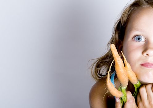 A sweet young girl eating fresh carrot. The child is on a white background