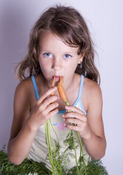 A sweet young girl eating fresh carrot. The child is on a white background