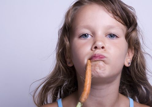 A sweet young girl eating fresh carrot. The child is on a white background