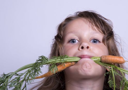 A sweet young girl eating fresh carrot. The child is on a white background