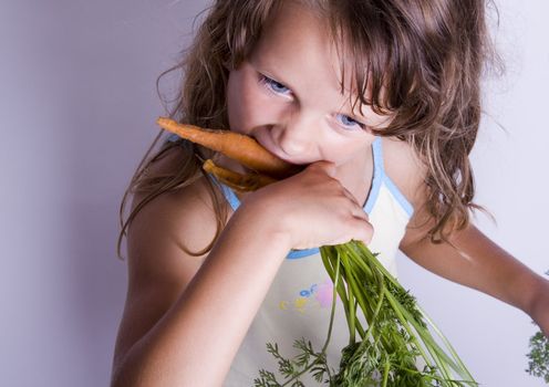 A sweet young girl eating fresh carrot. The child is on a white background