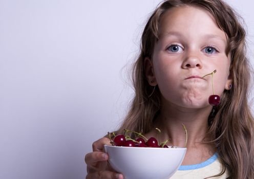 A sweet young girl eating fresh fruit. The child is on a white background