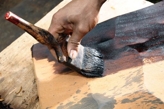 Close-up of a carpenter painting a wood slab.