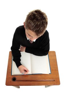 Conscientious school boy student sitting at a desk with an open book and pen in hand.