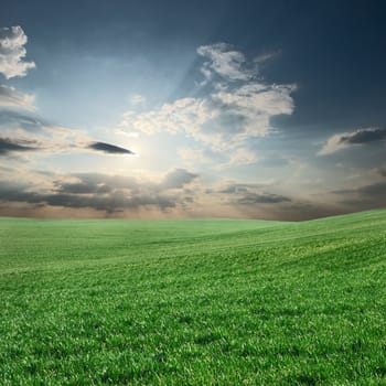 Green field with sunlight beams shining through the clouds