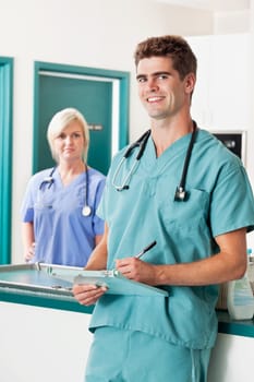 Portrait of smiling male veterinarian with clipboard while assistant in the background