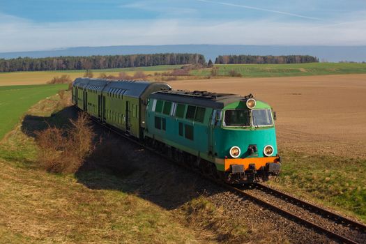 Passenger train hauled by the diesel locomotive passing the sunny landscape
