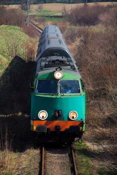 Passenger train hauled by the diesel locomotive passing the sunny landscape
