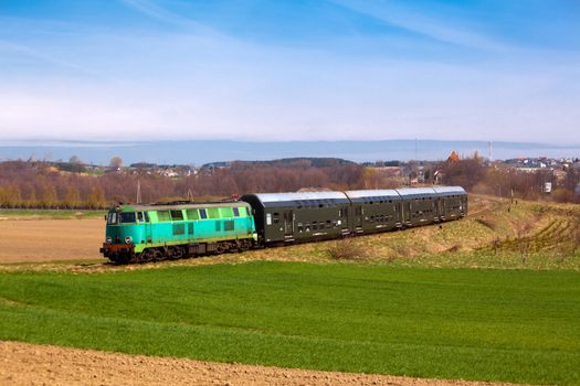 Passenger train hauled by the diesel locomotive passing the sunny landscape
