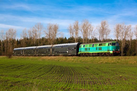 Passenger train hauled by the diesel locomotive passing the sunny landscape
