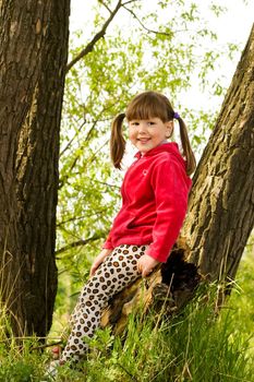 Smiling little girl sitting on tree in forest