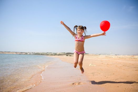 Girl jumping with balloon on the beach