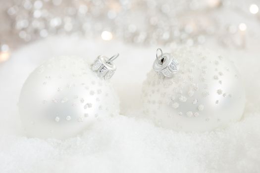 Pretty silver christmas baubles in the snow with lights in the background