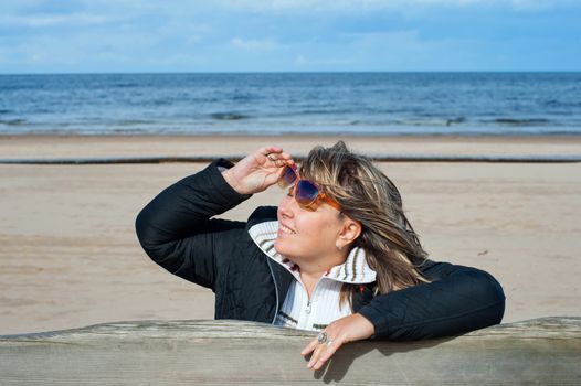 Portrait of mature woman in sunglasses relaxing at the Baltic sea in autumn day.