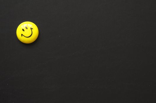 yellow smiley or smilie on black chalkboard with copyspace for a text message