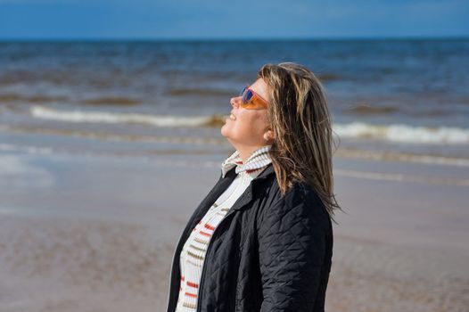 Portrait of mature woman in sunglasses relaxing at the Baltic sea in autumn day.