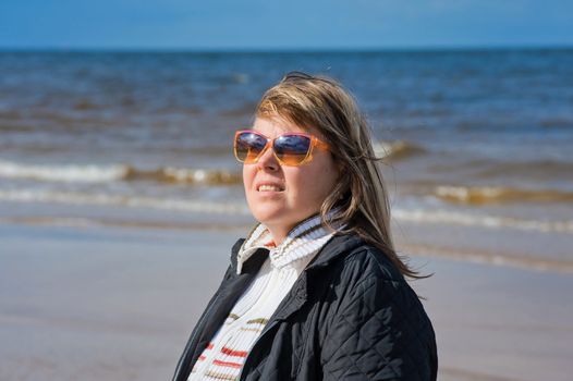 Portrait of mature woman in sunglasses relaxing at the Baltic sea in autumn day.