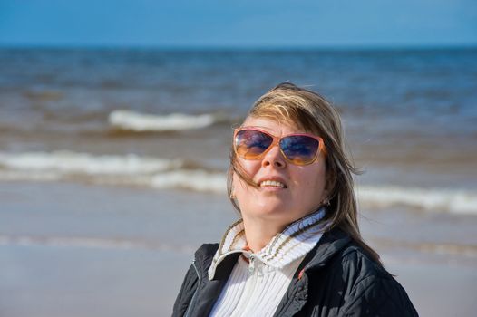 Portrait of mature woman in sunglasses relaxing at the Baltic sea in autumn day.