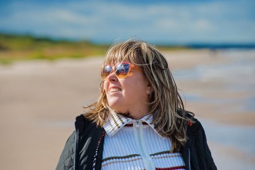 Portrait of mature woman in sunglasses relaxing at the Baltic sea in autumn day.
