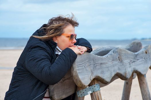 Thoughtful mature woman in sunglasses relaxing at the Baltic sea in autumn day.