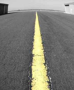 Black and white with single yellow punch on centerline of airport taxiway with fisheye distortion