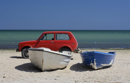 Two fishing boats and car standing on the sand of a beach