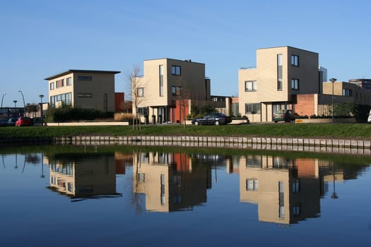 Three houses and their reflection in a pond in a modern suburb