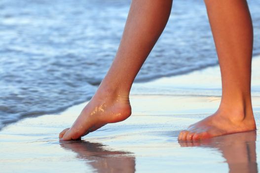 Feet of a young woman trying water on tropical beach