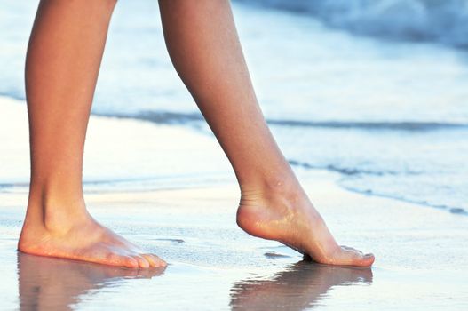 Feet of a young woman touching water on tropical beach