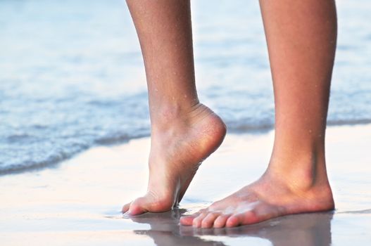 Feet of a young woman touching water on tropical beach