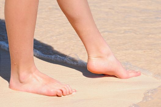 Feet of a young woman touching water on tropical beach